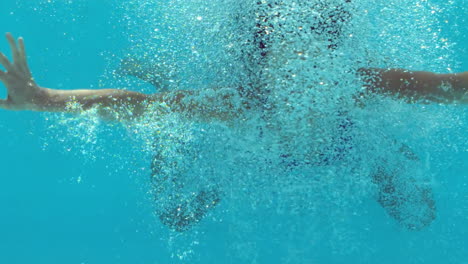 brunette woman floating underwater in blue bathing suit