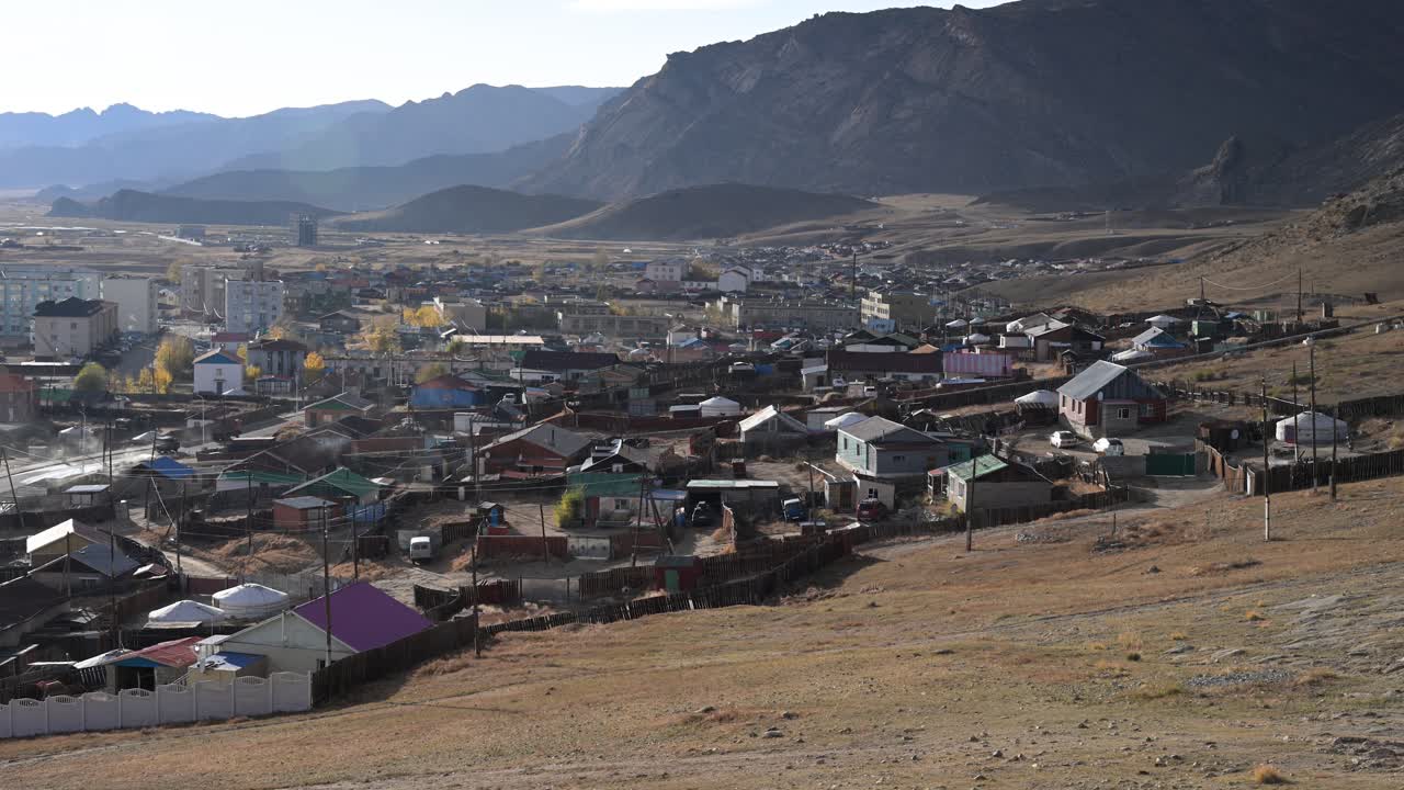A high-angle view of Uliastai, Mongolia, reveals a mix of traditional yurts (gers), colorful houses, and Soviet-era apartment blocks nestled in a vast, arid mountain valley