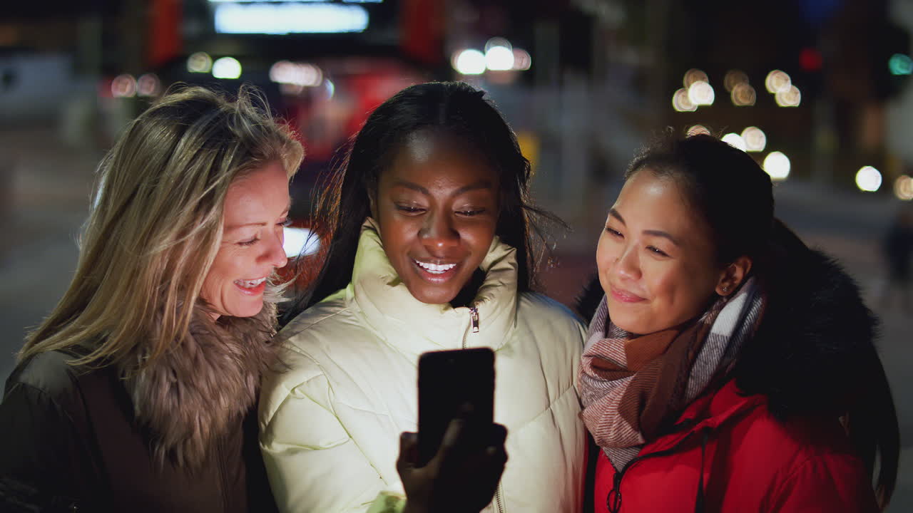 grupo de amigas en la calle de la ciudad por la noche pidiendo un taxi usando una aplicación de teléfono móvil