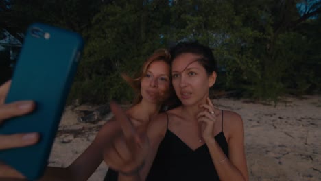 two women taking a selfie on a beach at sunset