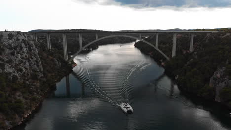 drone areal-lift shot of sailing boat driving under car bridge in fjord in croatia