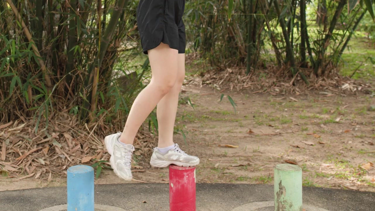 A woman performs balancing exercises on colorful posts in a sunny outdoor park setting