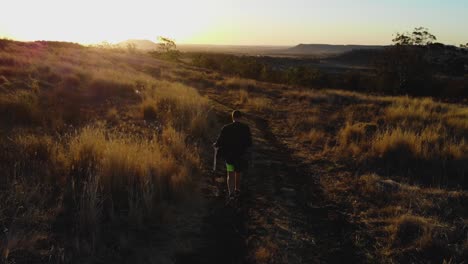 La-Cámara-Sigue-A-Un-Hombre-Mientras-Camina-Hacia-Una-Bella-Y-Cálida-Puesta-De-Sol-Con-Una-Moto-Al-Hombro