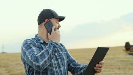 granjero con sombrero y hablando por teléfono mientras sostiene una tableta