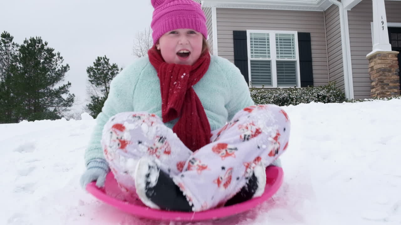 Slow motion shot of young girl sledding down a hill