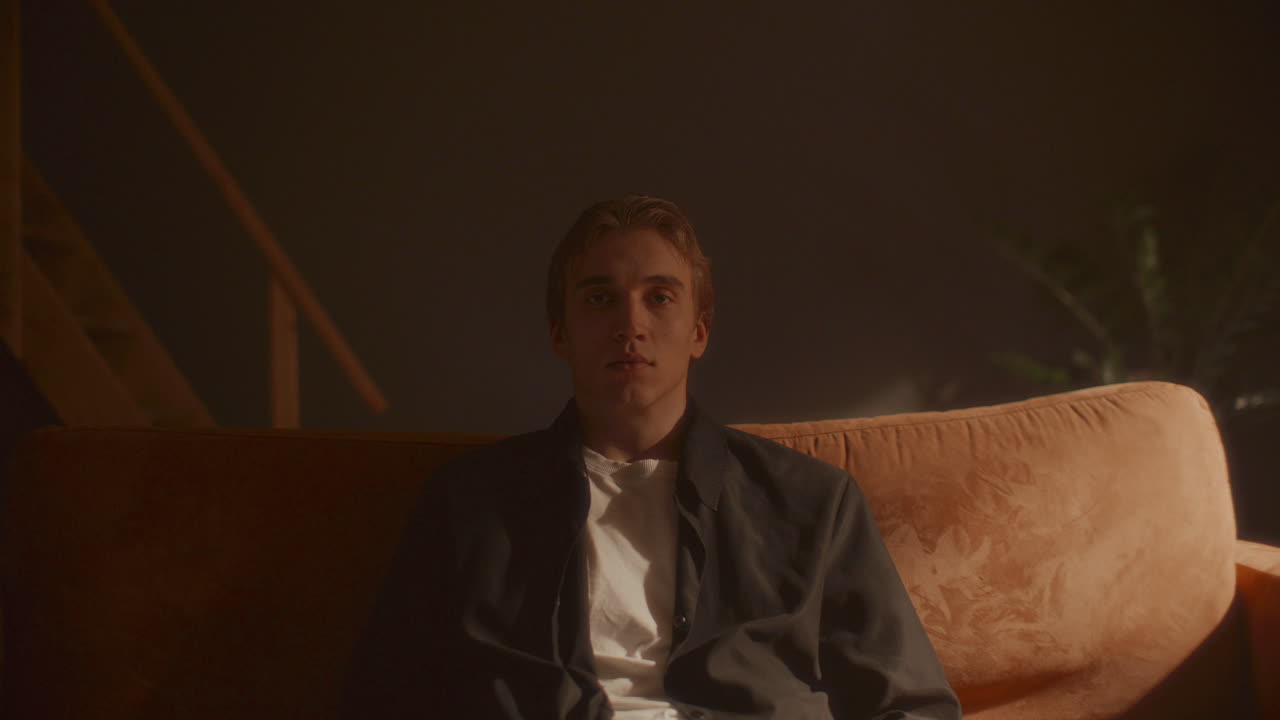 Portrait of Young Man Sitting Still on Sofa in Warmly Lit Room