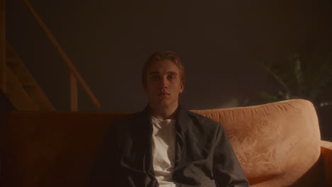 portrait of young man sitting still on sofa in warmly lit room