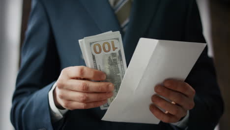 man taking money envelope indoors close up. hands holding american dollars.