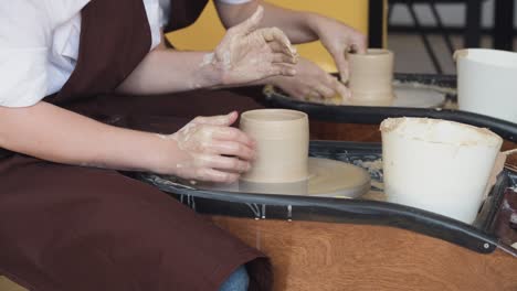 two women make pottery on a pottery wheels, shaping clay by their hands, close up. pottery craft workshop at art studio