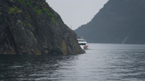 tourist boat disappearing behind coastal cliff in milford sound inlet