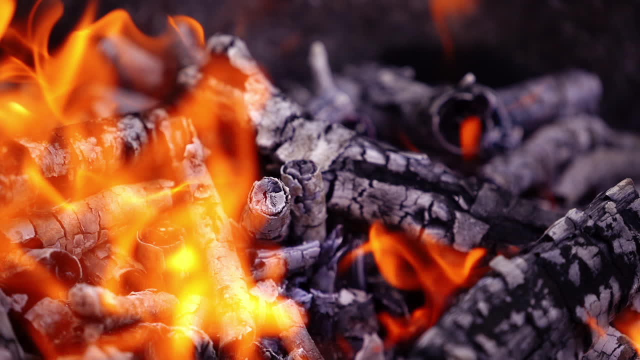 Smoldered wooden logs background. White ash from wood in fire. Detailed motion of slight flame over the charcoals. Close-up. Slow motion.