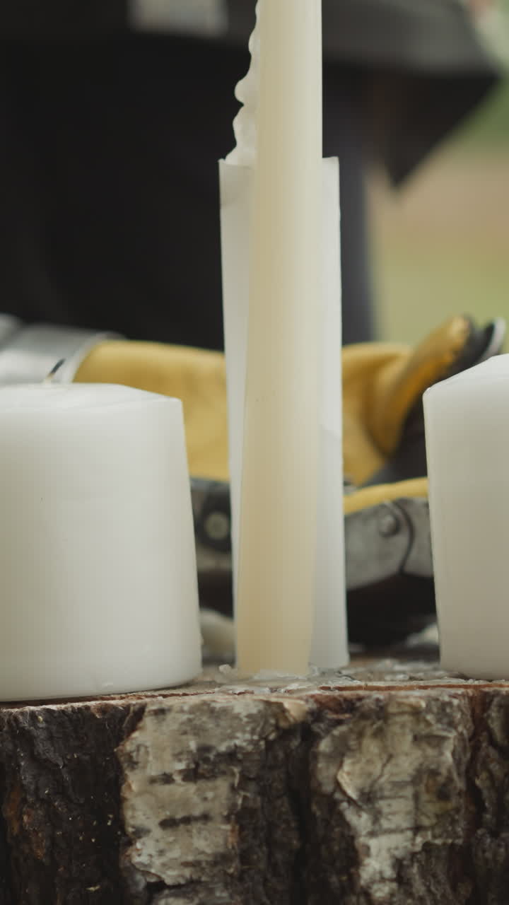 velas blancas de pie en el tronco seco en el césped. pareja de personas en ropa medieval de pie mirando objetos. mano femenina pone caballero guante de primer plano en fondo borroso