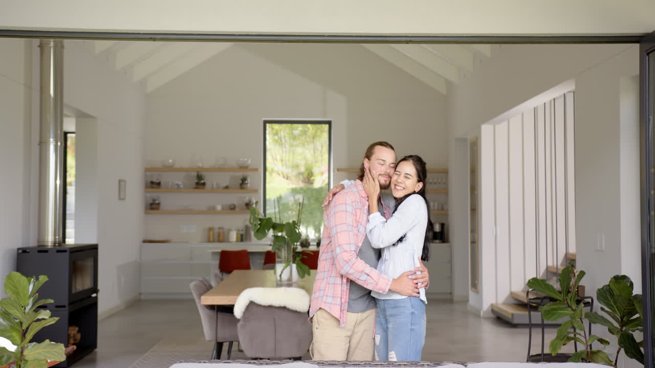 A biracial couple hugs warmly in a modern home