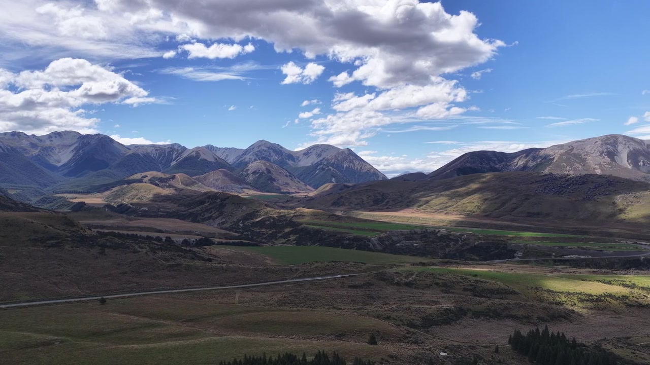 Un'ampia panoramica aerea dell'Isola del Sud della Nuova Zelanda rivela valli ondulate, catene montuose distanti e nuvole spettacolari che si muovono attraverso un vasto paesaggio aperto.