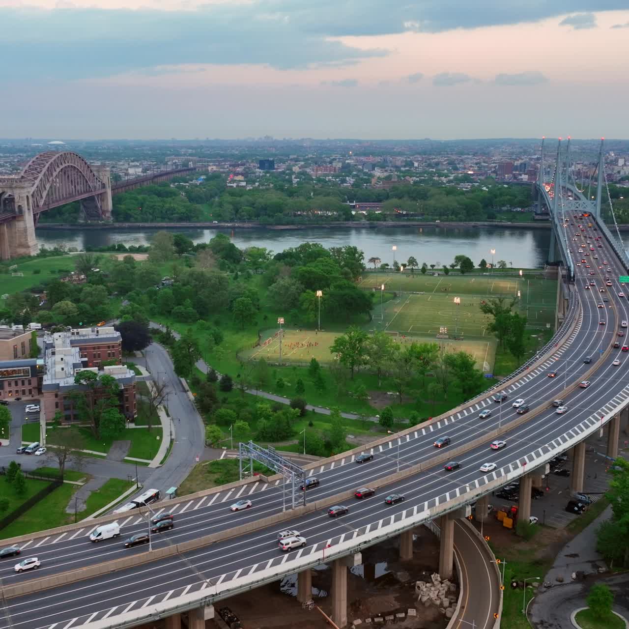 Two bridges nearby crossing New York river. Busy highway leading to the one of the bridges. Green parks and city at background