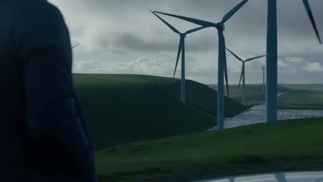 person overlooking a wind farm on rolling green hills under a cloudy sky