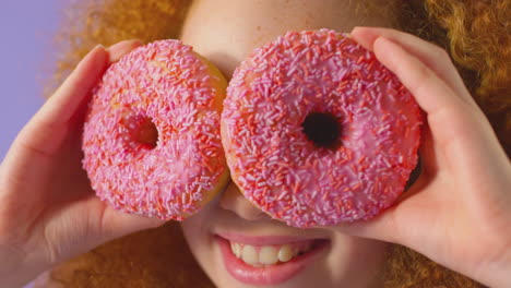 close up of girl holding two donuts in front of eyes against purple background