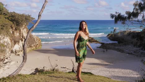 girl wearing green summer dress admiring scenic beach and ocean from headland park - islander at south gorge beach in point lookout, qld, australia