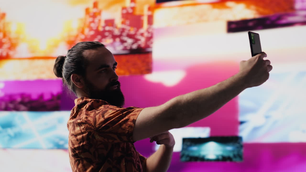 Young carefree man takes selfies and videos surrounded by fun neon lights