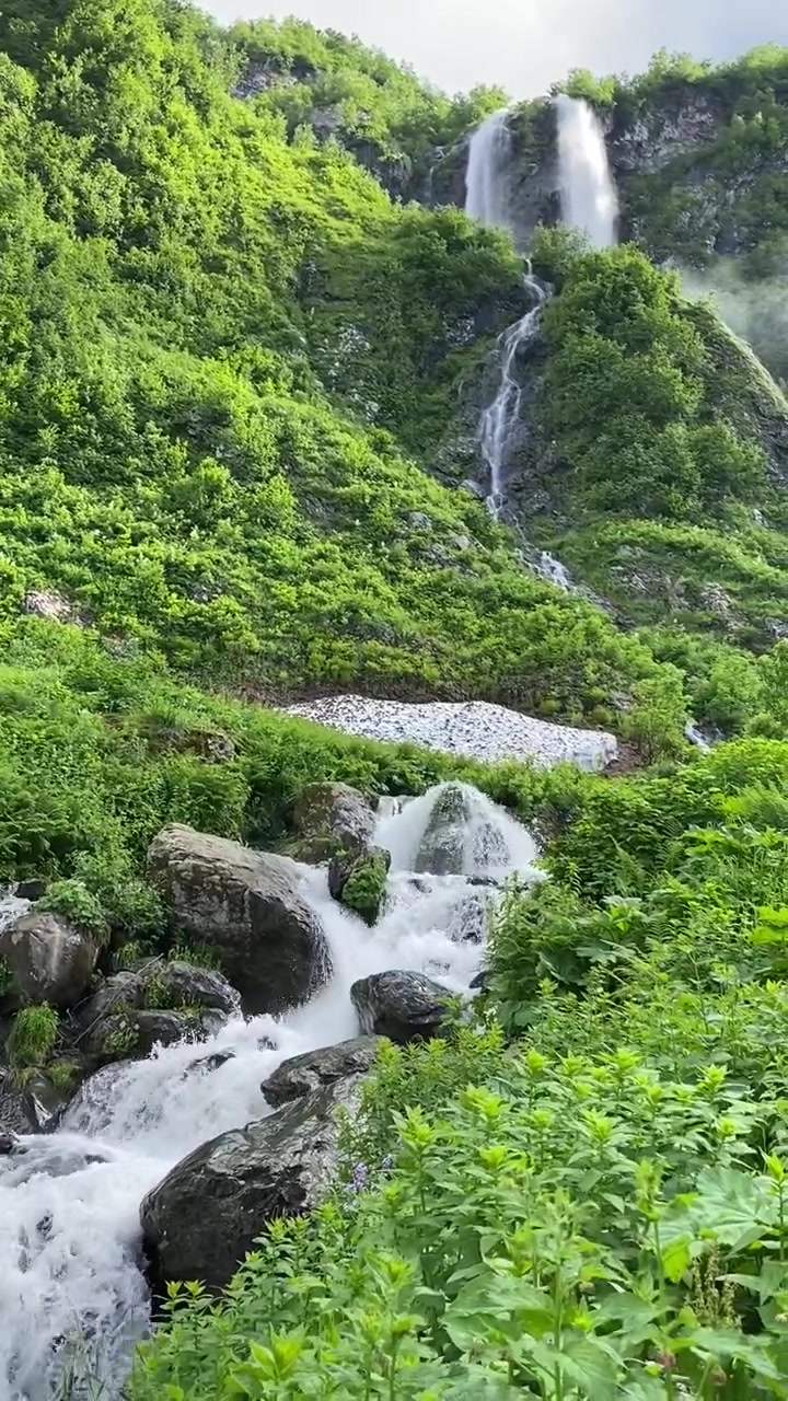 Pemandangan indah air terjun mengalir menuruni lereng gunung hijau di Maroko dengan vegetasi lebat, bebatuan, dan air segar menciptakan lanskap alam yang hidup.