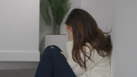 stressed or anxious woman sitting on floor leaning against wall at home reacting to internet or social media news message or story on mobile phone 1