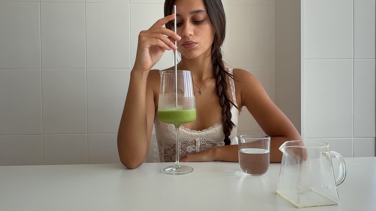 Giovane donna che mescola e beve una bevanda verde salutare