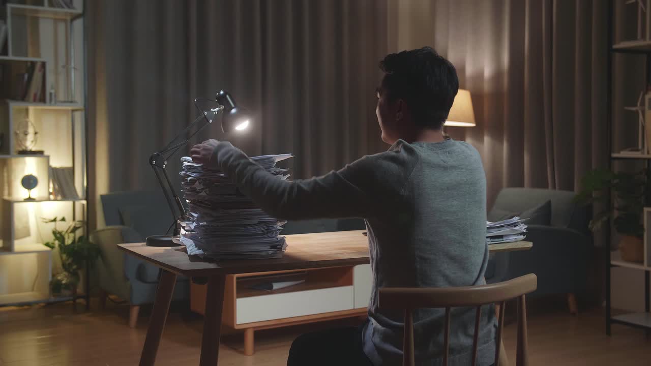 vista trasera de un hombre asiático feliz celebrando el final del trabajo con documentos en casa