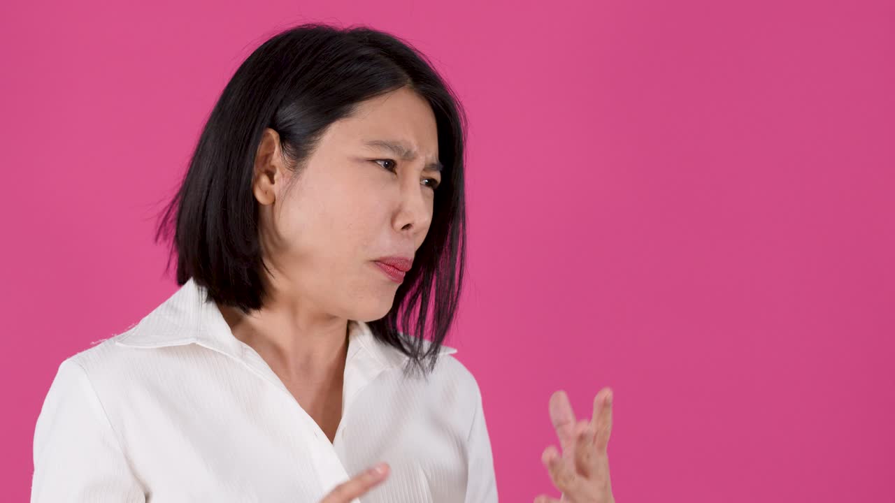 Một người phụ nữ châu Á thể hiện sự bối rối và lo lắng với hai lòng bàn tay mở trên nền hồng.