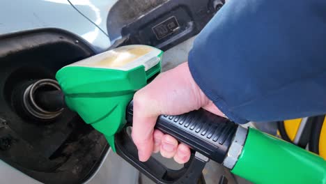 Primer-Plano-De-La-Mano-De-Una-Persona-Sosteniendo-La-Boquilla-De-La-Bomba-Verde,-Rellenando-El-Tanque-De-Gasolina-Del-Coche-Con-Combustible-En-La-Gasolinera