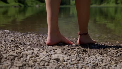a person’s bare feet on a rocky shore beside a calm lake on a sunny day in nature
