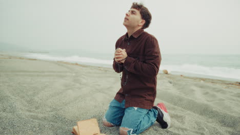 faithful man praying with passion with the bible book on the beach