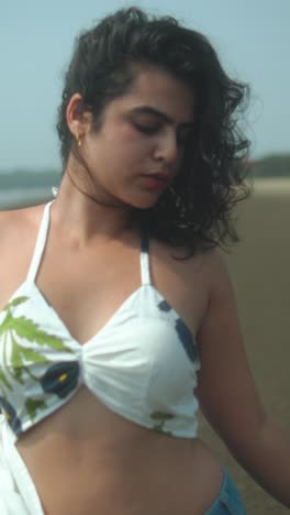confident young woman posing at beach, wearing summer outfit with natural expression