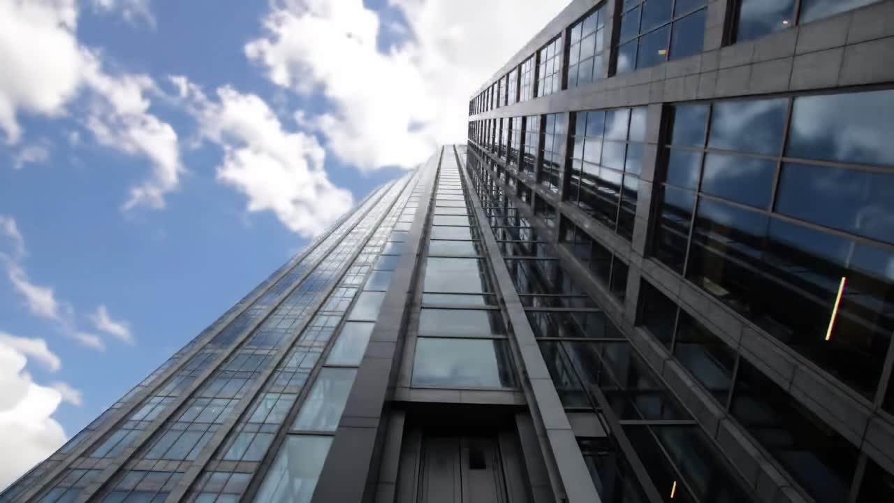 Looking up at a striking skyscraper showcases its sleek glass facade reflecting the clouds above. This architectural marvel stands tall in an urban environment, captivating passersby.