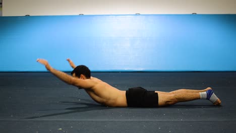 a guy doing an abs workout in a gymnastics gym doing lying down shortless leg and hand raises still shot