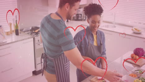 animation of hearts over diverse couple cooking together and drinking wine in kitchen at home