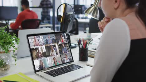 mujer caucásica teniendo una videoconferencia con colegas de oficina en una computadora portátil en la oficina