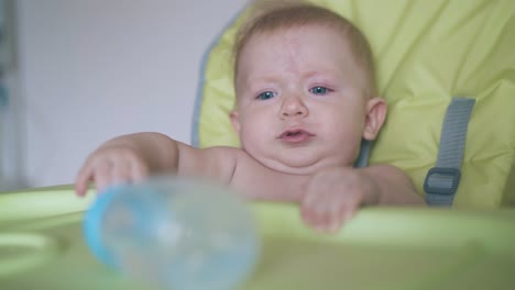 Un-Chico-Gracioso-Se-Sienta-En-Una-Trona-Con-Una-Botella-De-Agua-En-La-Mesa