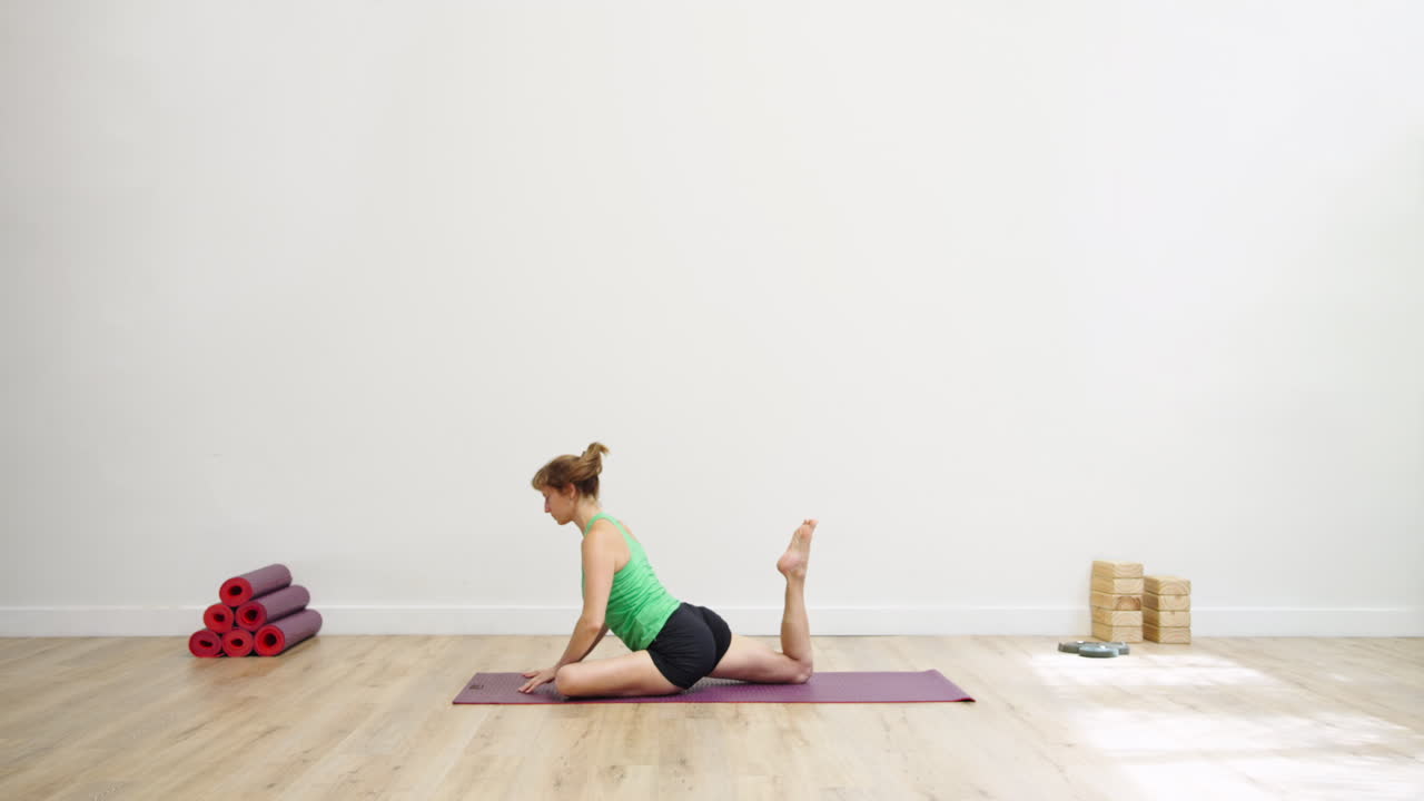 Woman Practicing Yoga Pigeon Pose and Seated Twist in Studio