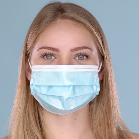 young woman posing in medical face mask  looking at camera with smile behind