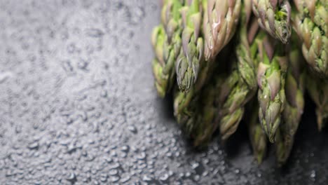 raw green asparagus on wet black slate background. rotating