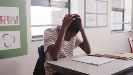 in school, african american teenage boy sitting at desk looking at wristwatch, focusing on time