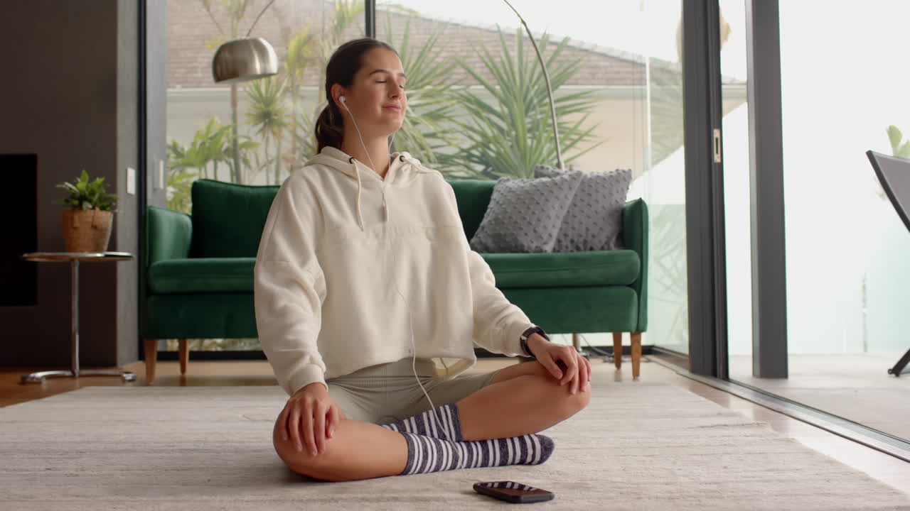 Meditating at home, woman sitting cross-legged with earphones and smartphone