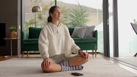 meditating at home, woman sitting cross-legged with earphones and smartphone