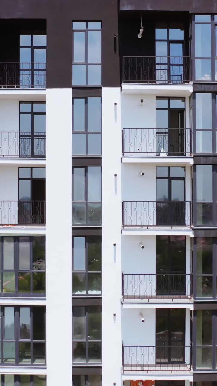 Black and white block of flats. Front view of a modern multi-storey building with glazed balconies in the city. Beautiful new housing apartments. Vertical video
