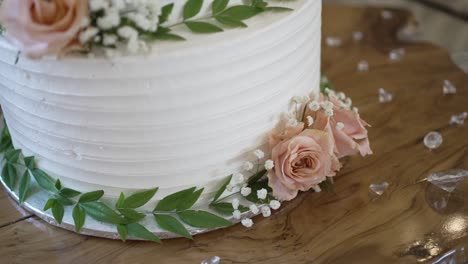 cerca de un pastel de boda blanco decorado con rosas rosas y hojas verdes