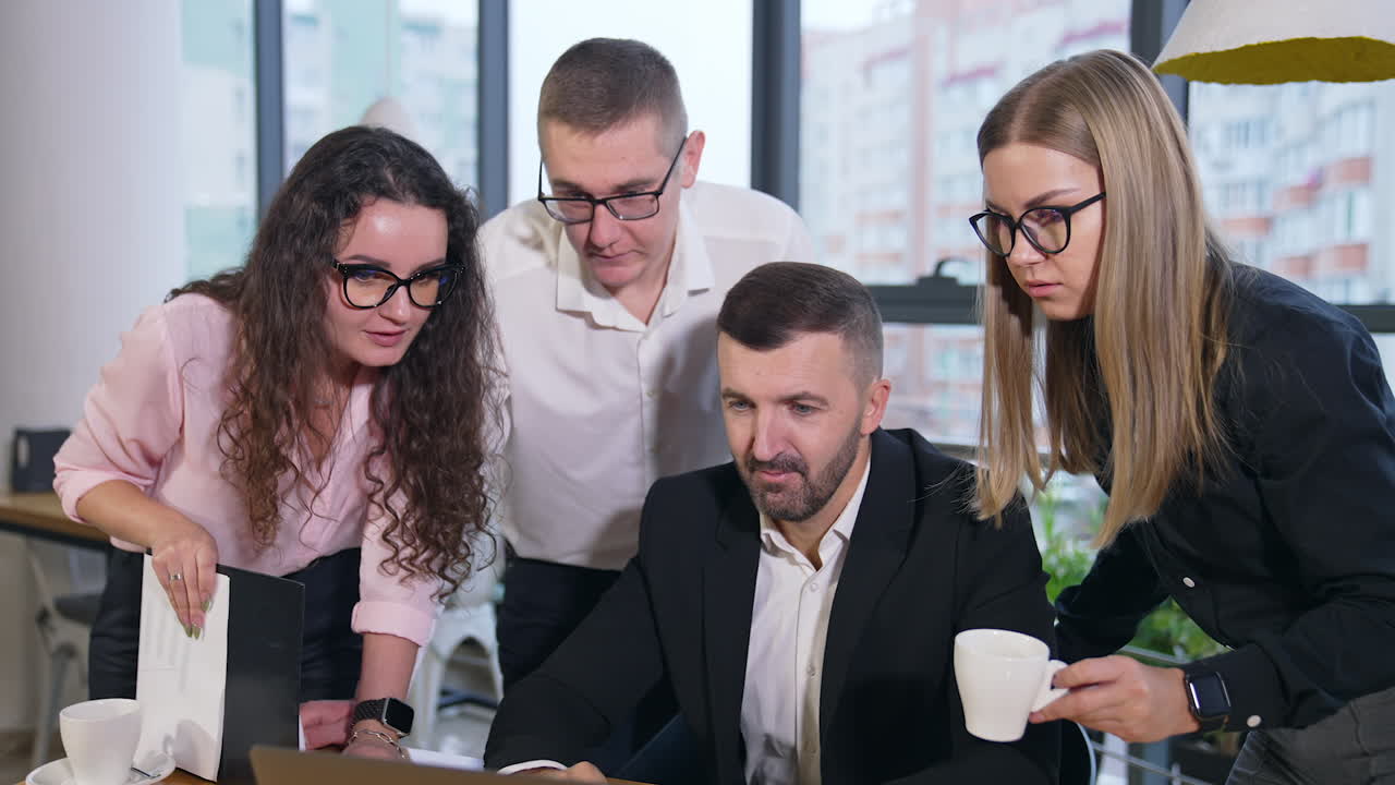Co working of colleagues in the spacious office. All teammates gathered to look at laptop standing in front of boss.