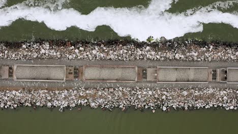 freight train transports stone by wavy water, rising top down aerial