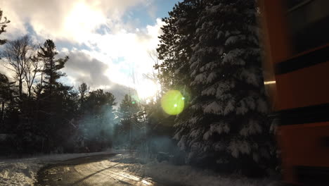 Tiro-Exterior-De-Invierno-Durante-El-Día-Que-Se-Inclina-Hacia-Abajo-Desde-árboles-Nevados-Para-Revelar-Un-Autobús-Escolar-De-Ontario-Conduciendo-Por