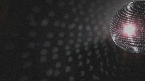 animación de un punto de luz rosa sobre una pelota de discoteca giratoria contra partículas blancas sobre un fondo negro.