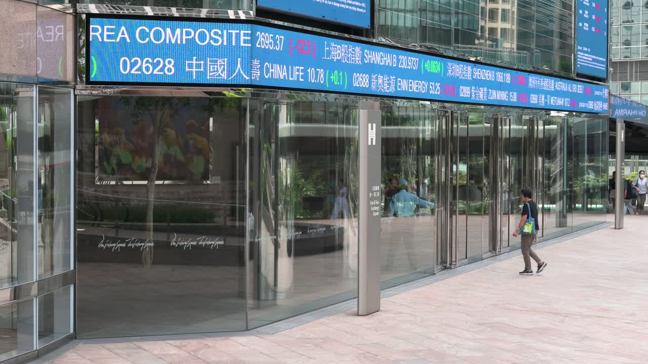 A woman enters the Exchange Square building, home to the Hong Kong Stock Exchange (HKEX), as a moving screen displays negative stock ticker symbols in Hong Kong’s financial district.